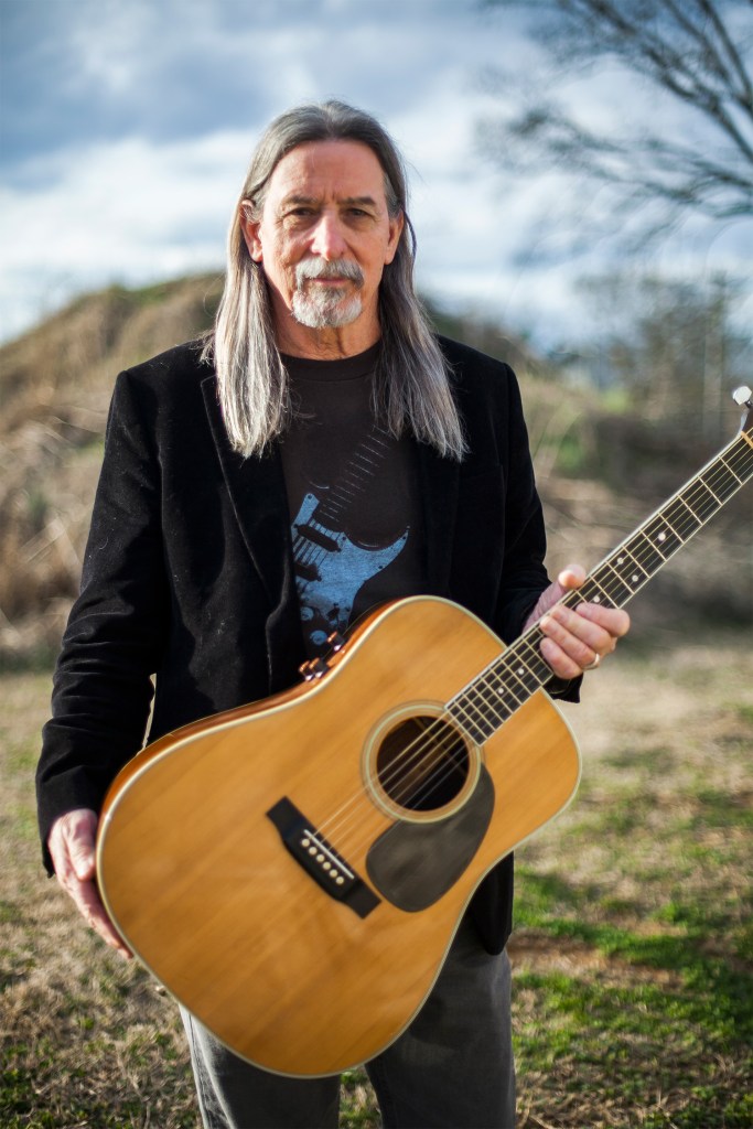 picture of John standing with a guitar
